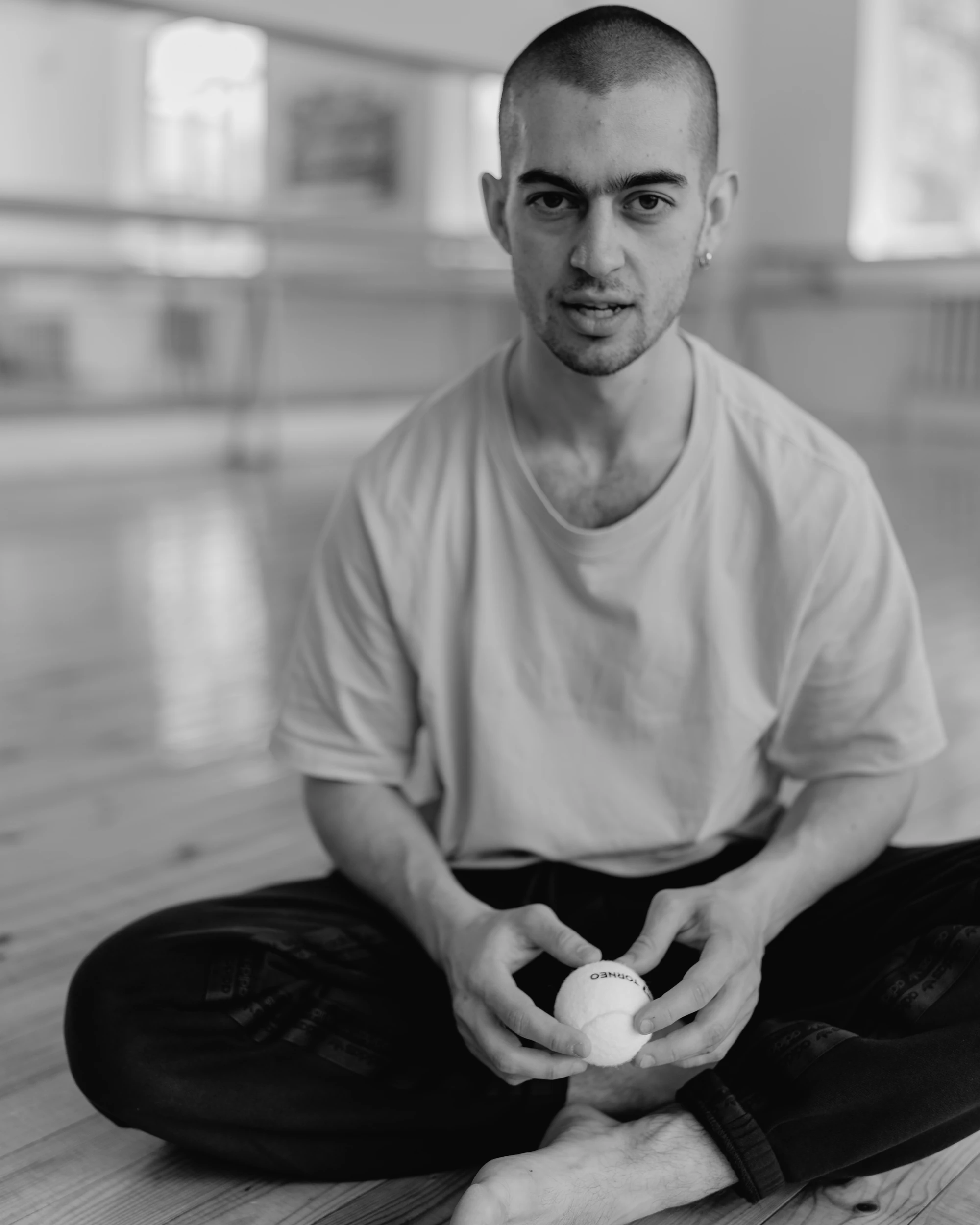 Black-and-white portrait of Kolya Bagdasaryan seated on a studio floor and holding a small ball.