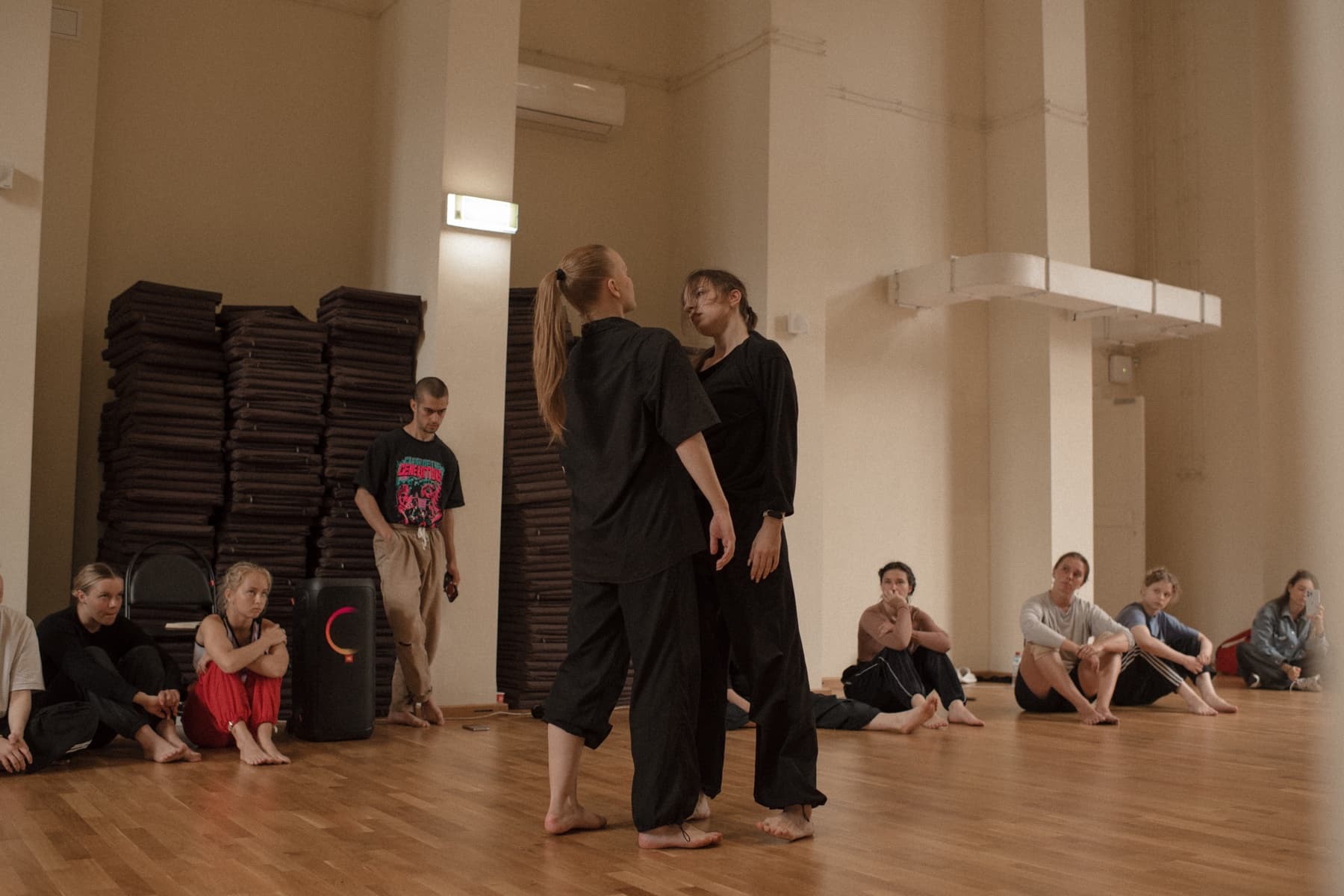 Two performers meeting in the centre of a studio while the Green Theatre group observes from the floor.