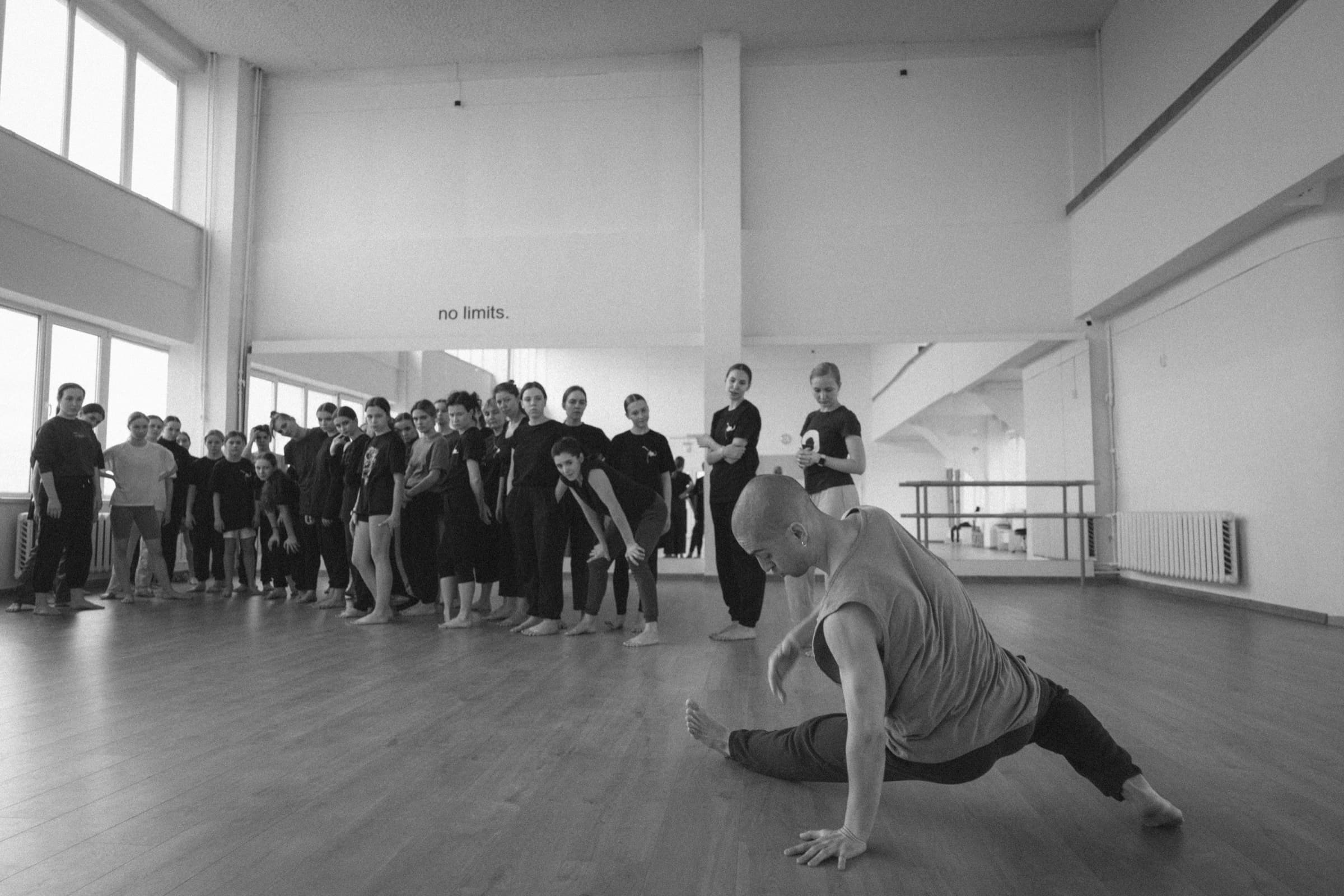 A workshop facilitator demonstrates a floor movement while participants observe together in the studio.