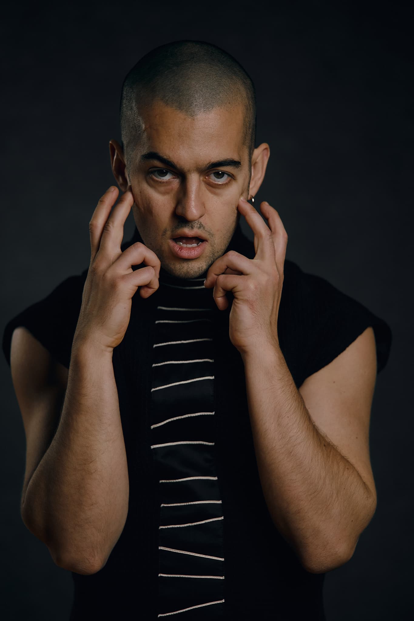 Kolya Bagdasaryan as Mephistopheles in a dark costume, holding both hands beside his face.
