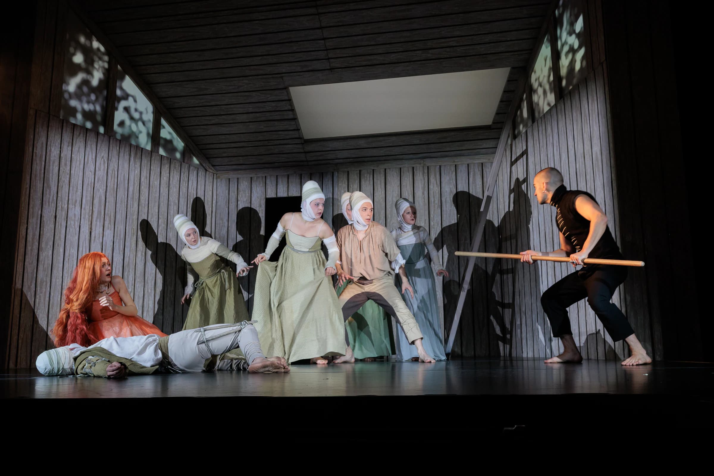 Mephistopheles confronts an ensemble of performers in a wooden stage interior.