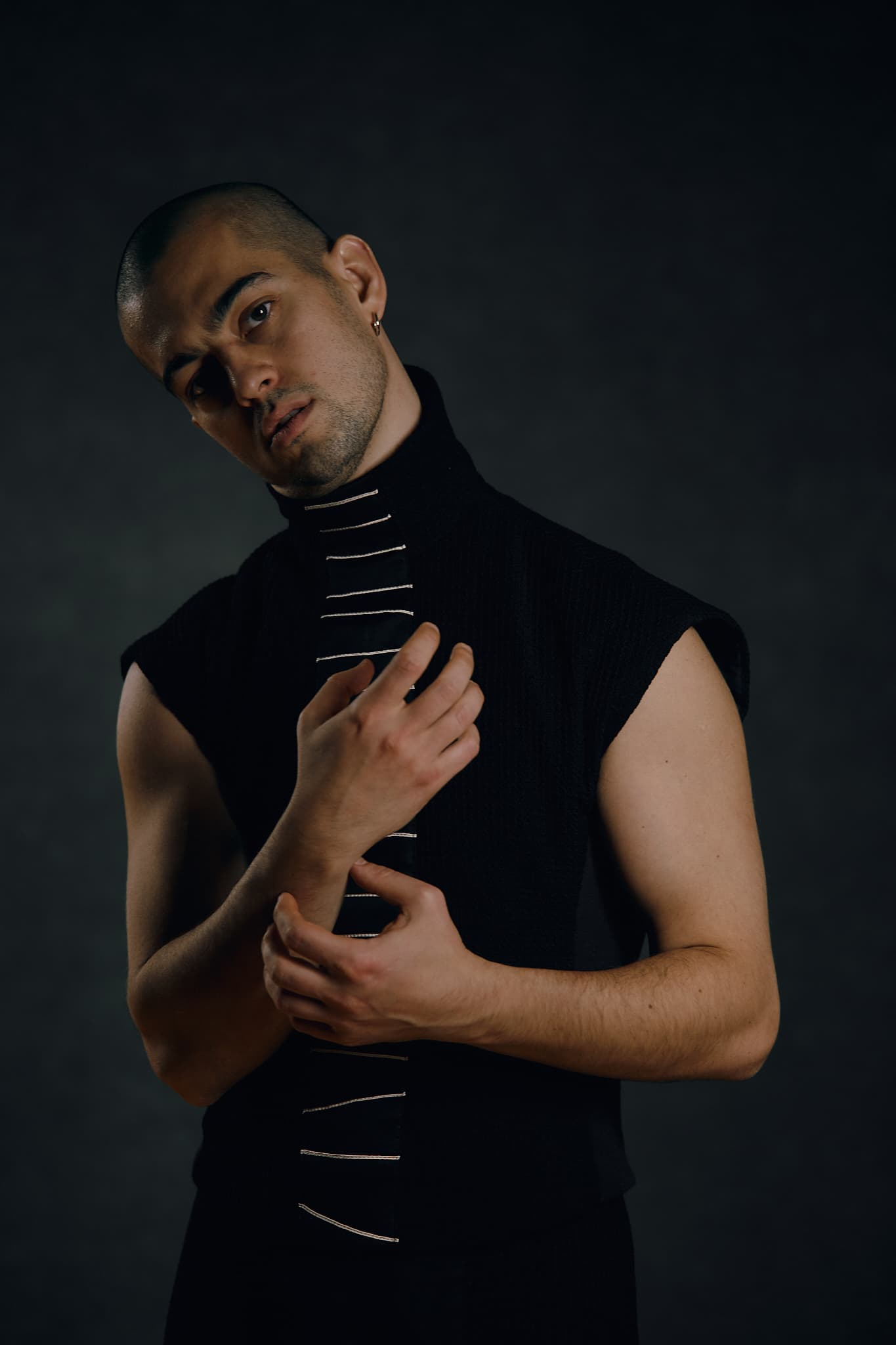 Kolya Bagdasaryan as Mephistopheles in a black costume, head tilted and one hand holding the opposite wrist.