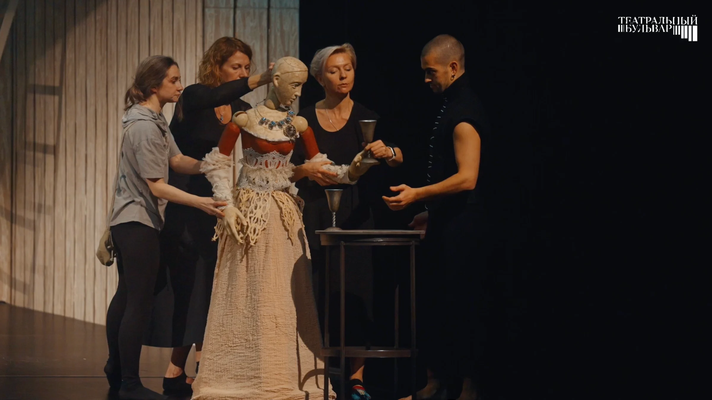The creative team rehearses with a puppet while Mephistopheles stands beside the scene.