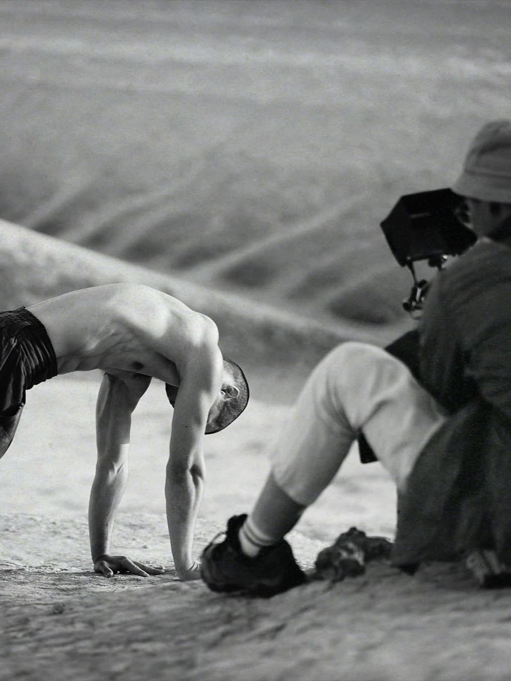 Backstage view of Kolya Bagdasaryan arching toward the ground while a camera operator films him in Bozzhyra.
