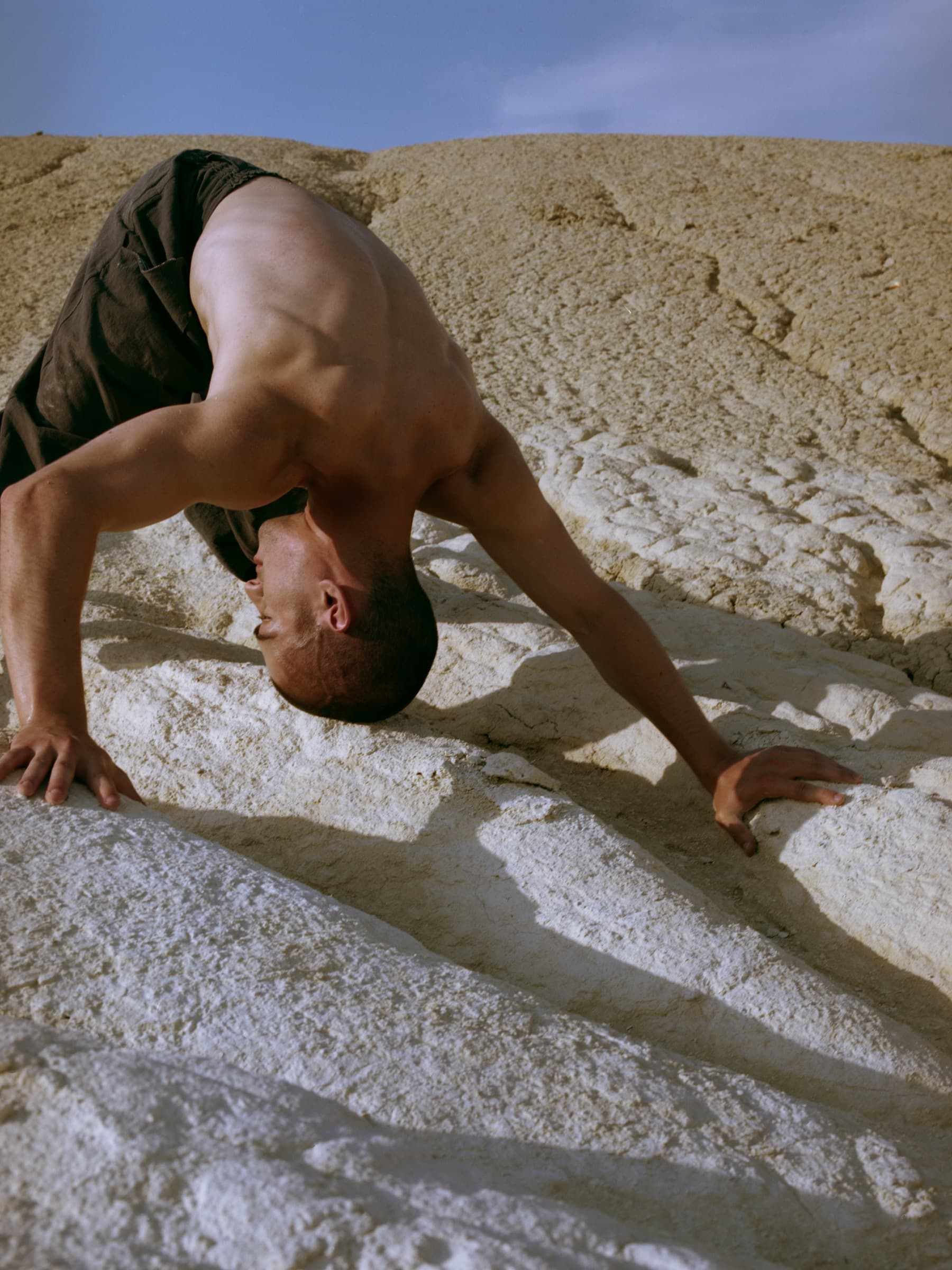 Kolya Bagdasaryan folding backward with both hands grounded against the pale Bozzhyra landscape.